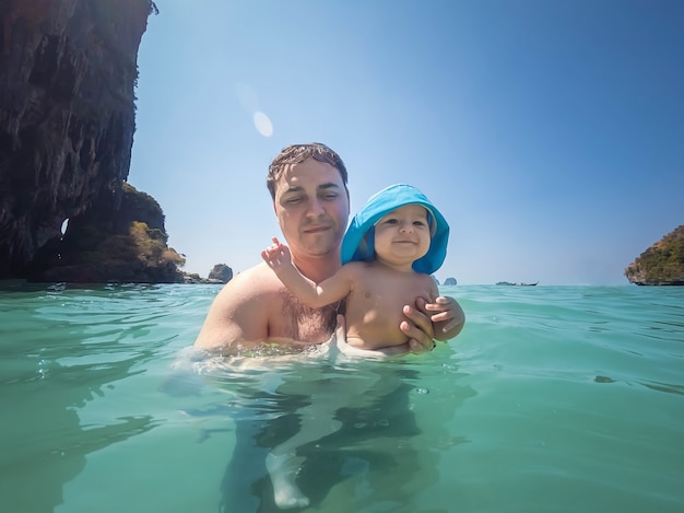 Ein glückliches Baby von sieben Monaten badet zum ersten Mal im Meer Sonniger Tag Papa hält das Baby