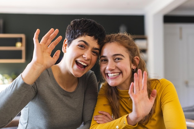 Ein glückliches bi-rassisches lesbisches Paar sitzt zu Hause bei einem Videoanruf und winkt