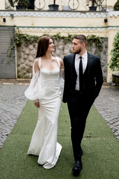 Ein glückliches Ehepaar geht auf den Straßen und umarmt sich in einem eleganten weißen Kleid und einem schwarzen Anzug