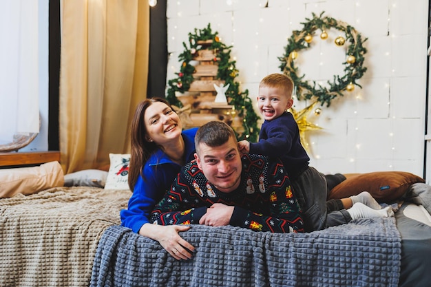 Ein glückliches Familienpaar mit einem Kind an Neujahrsorten. Neujahrsfeststimmung im Familienkreis. Weihnachtsdekoration im Schlafzimmer. Neujahrsweihnachtsdekoration zu Hause