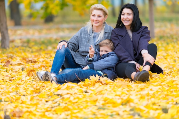 Ein glückliches gleichgeschlechtliches weibliches Paar und ihr Sohn in einem glücklichen Familienthema mit gelben Herbstblättern.