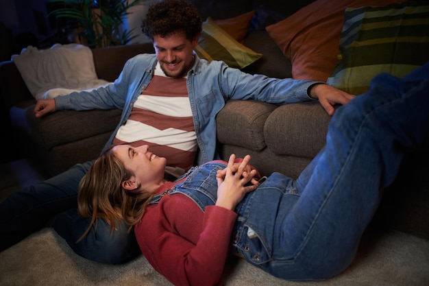 Ein glückliches junges, erwachsenes, kaukasisches, verliebtes Paar plaudert liebevoll und sitzt abends zu Hause auf dem Teppich.