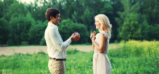 Ein glückliches junges Paar heiratet. Ein Mann schlägt seiner geliebten Frau im Sommerpark einen Ring vor.