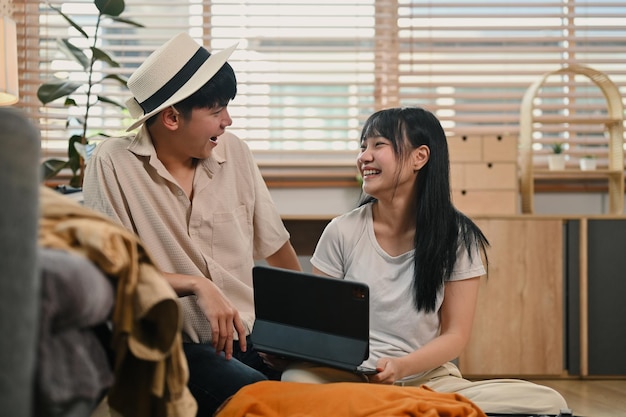 Ein glückliches junges Paar redet fröhlich, während es zusammen im Wohnzimmer einen Koffer für den Urlaub packt