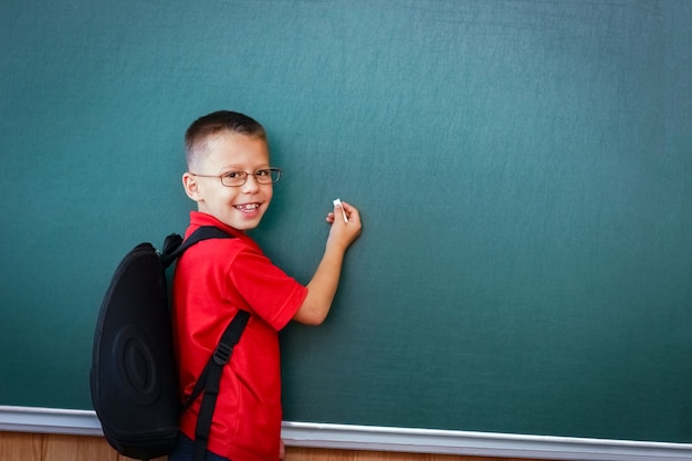 Ein glückliches Kind steht an der Tafel mit einem Schulrucksack mit Brille