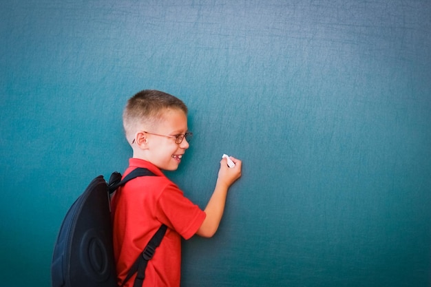 Ein glückliches Kind steht an der Tafel mit einem Schulrucksack mit Brille