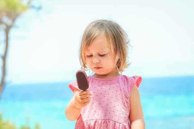 Ein glückliches Kindermädchen mit Eis am Meer in der Natur in der Parkreise