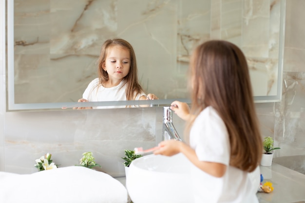 Ein glückliches kleines Mädchen putzt sich vor einem Spiegel im Badezimmer die Zähne. Morgenroutine. Hygiene. Foto in hoher Qualität