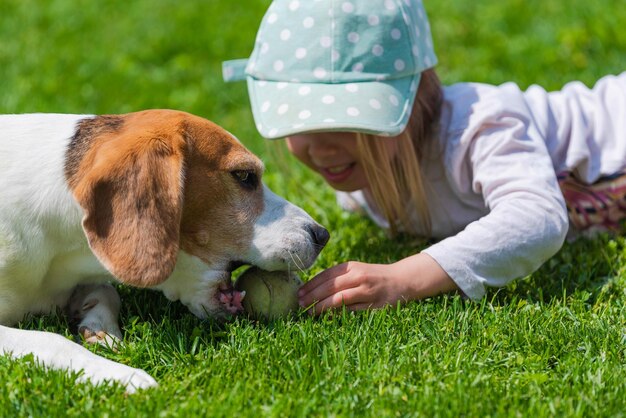 Ein glückliches kleines Mädchen spielt mit einem Beagle-Hund im Garten