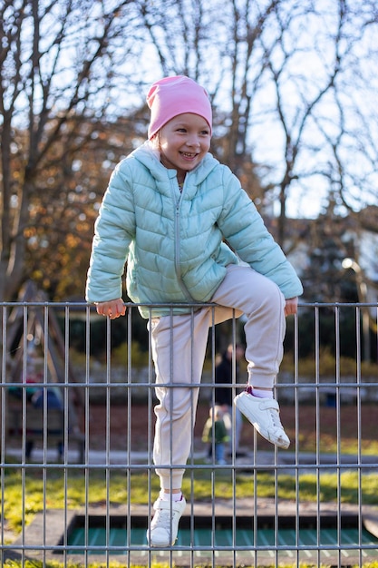Ein glückliches kleines Mädchen spielt, über den Eisenzaun auf der Straße zu klettern