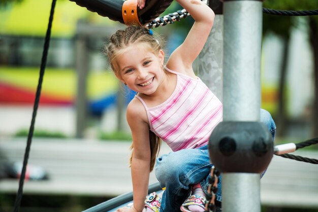 Ein glückliches, lächelndes kleines Mädchen spielt im Freien auf dem Spielplatz