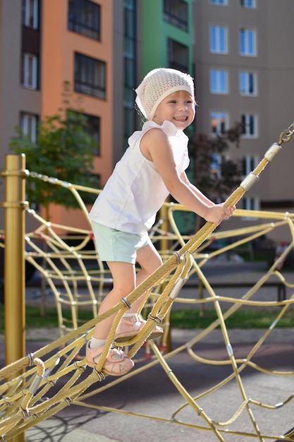 Ein glückliches Mädchen, das in einem Seilnetz auf dem Spielplatz spielt Moderner Spielplatz Aktive Erholung in der Stadt