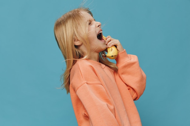 Foto ein glückliches mädchen hält eine banane vor blauem hintergrund