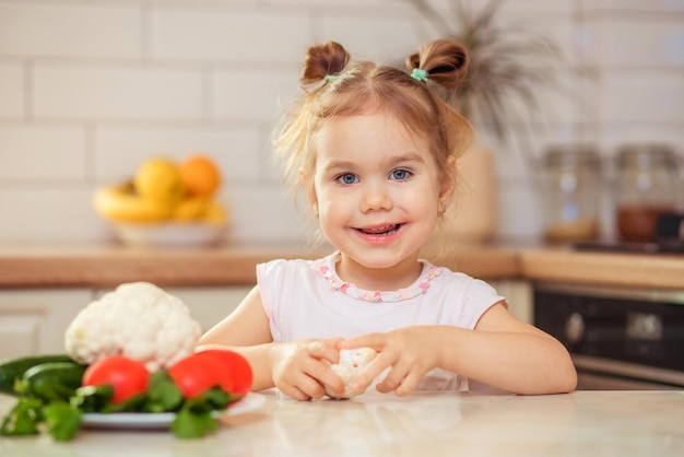 Ein glückliches Mädchen im Alter von 23 Jahren in der Küche zu Hause oder im Kindergarten isst leckeres und gesundes Gemüse zum Mittagessen