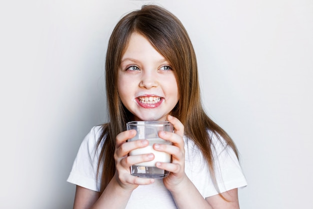 Ein glückliches Mädchen mit einem Glas Milch, das fröhlich mit Milch auf den Lippen lächelt