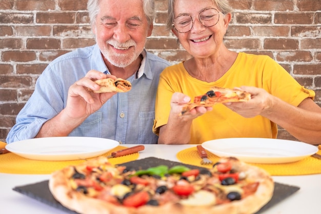 Ein glückliches Seniorenpaar, das bereit ist, ein Stück Pizza zu beißen. Eine Frau und ein Mann teilen sich eine traditionelle italienische Pizza.