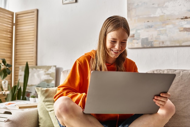 ein glückliches Teenager-Mädchen mit einem Laptop, das ihre Zeit genießt und auf dem Sofa im Wohnzimmer sitzt