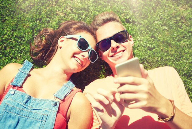 Foto ein glückliches teenagerpaar mit smartphone, das auf dem gras liegt