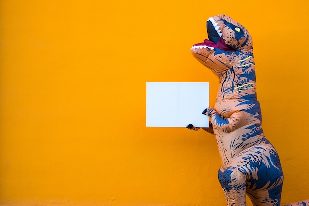 Ein glückliches und lustiges Dinosaurier-Kostüm tanzt auf der Straße mit einem orangefarbenen Hintergrund Trex macht Spaß lustiger Mann in einem Kostüm von DinoxA