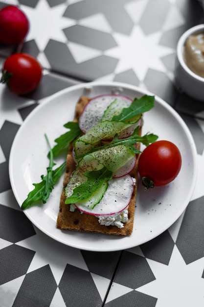 Ein grauer Teller mit einem Sandwich mit Buko-Käse, Rettich und Oruguts auf einem bunten Grafiktisch (asiatischer, südlicher Stil). Ein gesundes Frühstück mit Gemüse und Kräutern. Schöner Snack