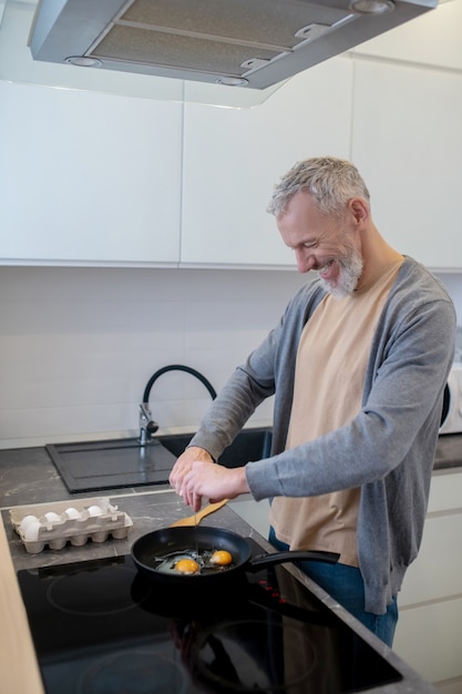 Ein grauhaariger mann, der in der küche omelette kocht