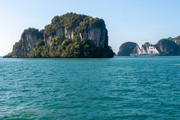 Ein großer Felsen im türkisfarbenen Meer und ein weißes Segelboot in der Nähe