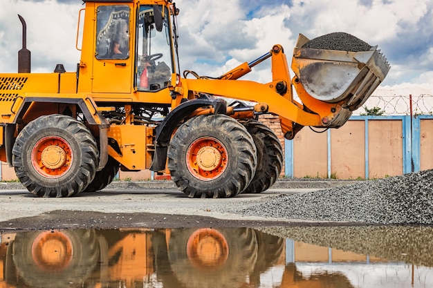 Ein großer Frontlader transportiert Schotter oder Kies in einem Eimer auf einer Baustelle oder einem Betonwerk Transport von Schüttgütern Baumaschinen Transport von Schüttgütern