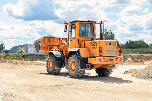 Ein großer Frontlader transportiert Schotter oder Kies in einem Eimer auf einer Baustelle oder einem Betonwerk Transport von Schüttgütern Baumaschinen Transport von Schüttgütern