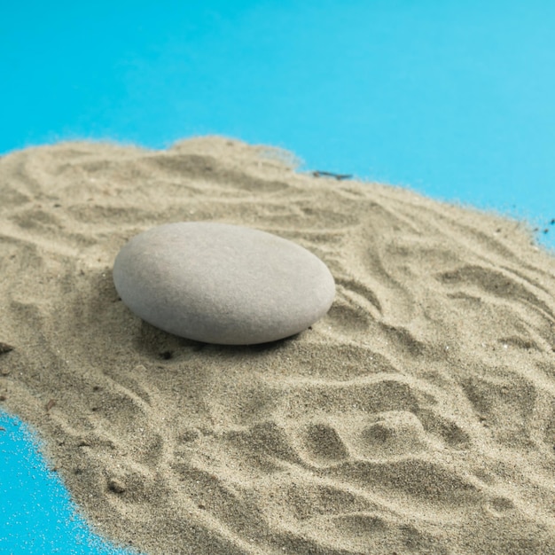 Ein großer grauer Stein auf dem grauen Sand auf blauem Hintergrund