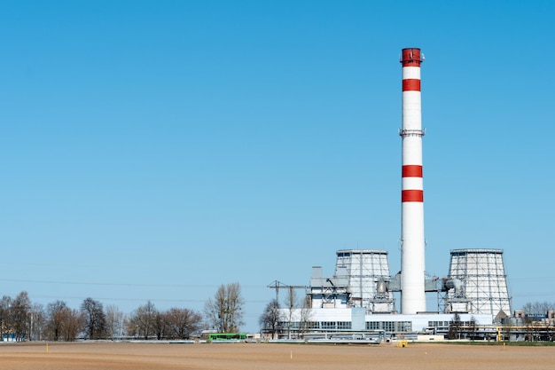 Ein großer industrieller Schornstein vor blauem Himmel Rote und weiße Rohre in Gewerbebetrieben oder Kraftwerken