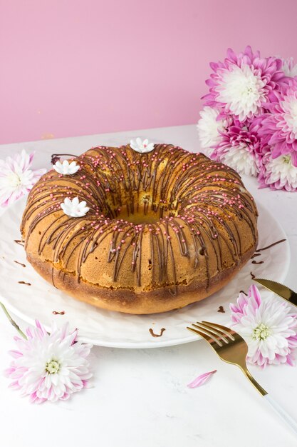 Ein großer kleiner Kuchen gegen eine Chrysantheme. Ein kleiner Kuchen mit Orangen und kandierten Früchten. Schokoladenganache und weiße Zuckergänse. Vertikale Ausrichtung