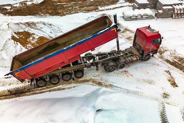 Ein großer Muldenkipper entlädt im Winter Bauschutt oder Kies auf einer Baustelle Autotonar für den Transport schwerer Schüttgüter Versorgung der Baustelle mit Materialien Bauen im Schnee