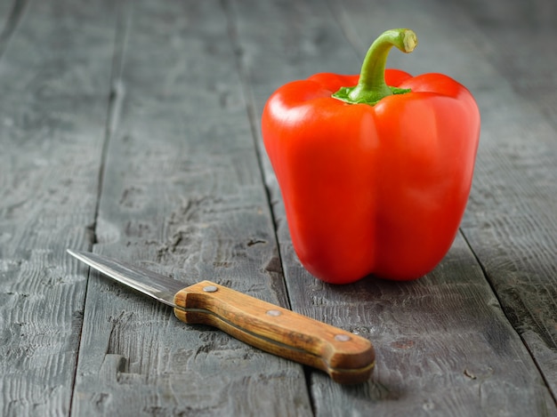 Foto ein großer roter grüner pfeffer mit einem messer auf einer schwarzen rustikalen tabelle. vegetarisches essen.