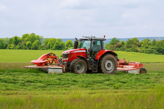 Ein großer roter Traktor mit zwei Mähern mäht das grüne Gras auf einem Silo.