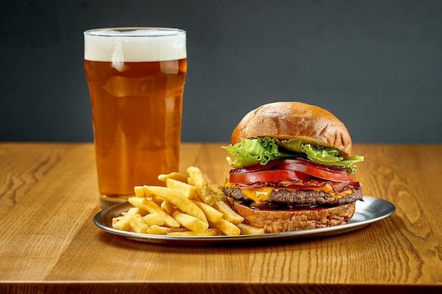 Ein großer saftiger Burger mit Gemüse und einem Glas Bier Selektiver Fokus der Nahaufnahme