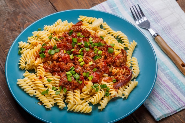 Ein großer Teller Bolognese-Nudeln in Tomaten mit Frühlingszwiebeln auf einem Holztisch