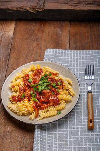 Ein großer Teller Bolognese-Nudeln mit Frühlingszwiebeln auf einem Holztisch auf einer Serviette