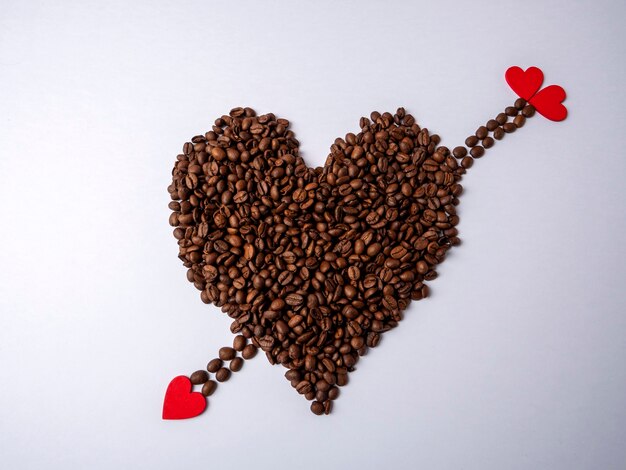 Ein großes braunes Herz aus Kaffeebohnen und ein brauner Pfeil mit roten herzförmigen Spitzen durchbohren es gegen ein strahlendes Weiß
