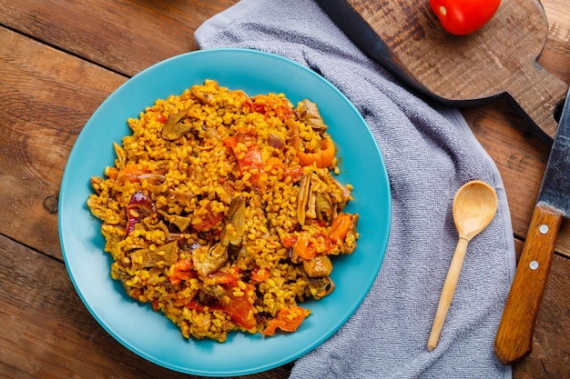 Ein großes Bulgurgericht mit Gemüse und Pilzen in Gewürzen auf dem Tisch auf einer blauen Serviette neben Tomaten und Zwiebeln