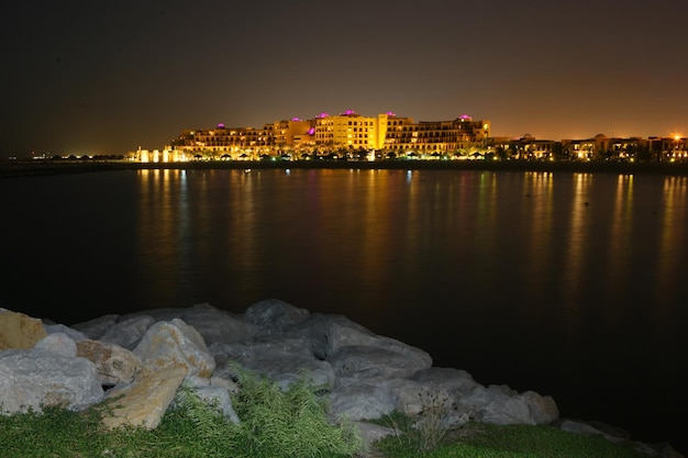 Ein großes Hotel ist nachts mit ruhigem Meer und Felsen im Vordergrund beleuchtet