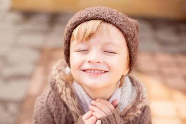 Ein großes Porträt eines kleinen glücklichen Jungen mit einem breiten Lächeln und großen Augen in einer Strickmütze