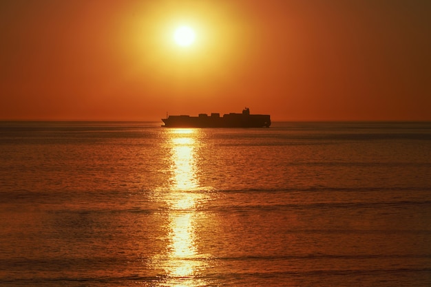 Ein großes schiff am horizont im atlantik unter der hellen sonne und dem roten sonnenuntergang. sonnenlichtreflexion vom wasser