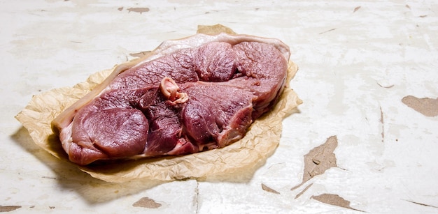 Ein großes Stück rohes Schweinefleisch auf Papier auf rustikalem Hintergrund