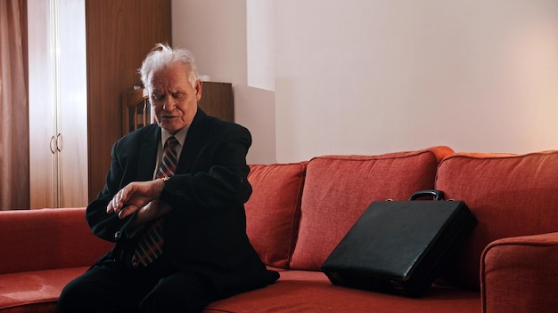 Ein Großvater eines alten Mannes, der auf dem Sofa sitzt und auf seine Handuhr schaut
