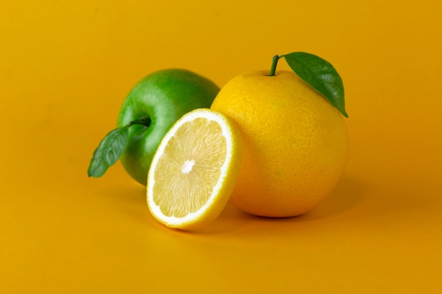 Ein grüner Naturapfel mit gelben Zitronenfrüchten und eine Zitronenscheibe mit Blatt auf gelbem Hintergrund