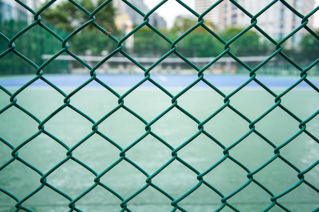 Ein grünes Stahlnetz, das sich am Zaun des Tennisplatzes verhakt