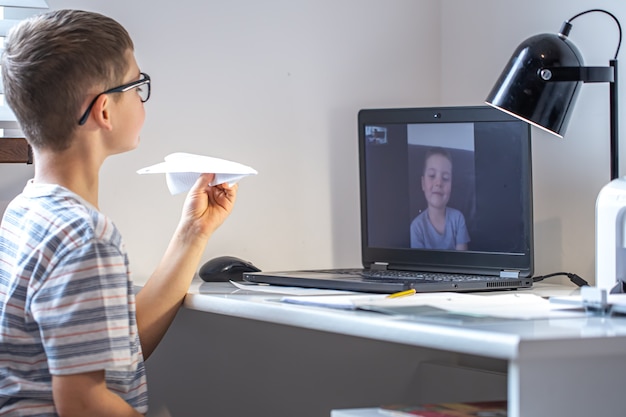 Ein Grundschüler sitzt an einem Schreibtisch vor einem Laptop und kommuniziert zu Hause per Videoverbindung online.