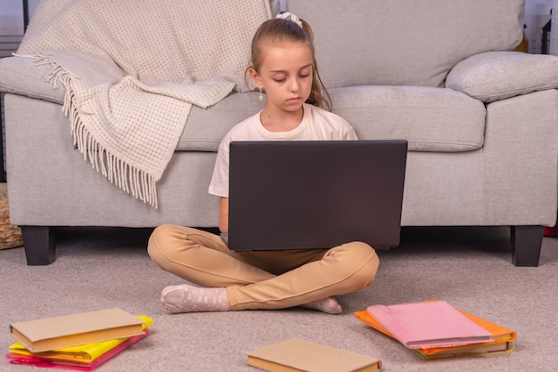 Ein Grundschulmädchen sitzt mit einem Laptop zu Hause auf der Couch im Online-Unterricht