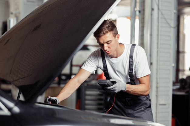 Ein gut aussehender blonder Mechaniker in Uniform überprüft bei einem Autoservice die Blinker eines Fahrzeugs.