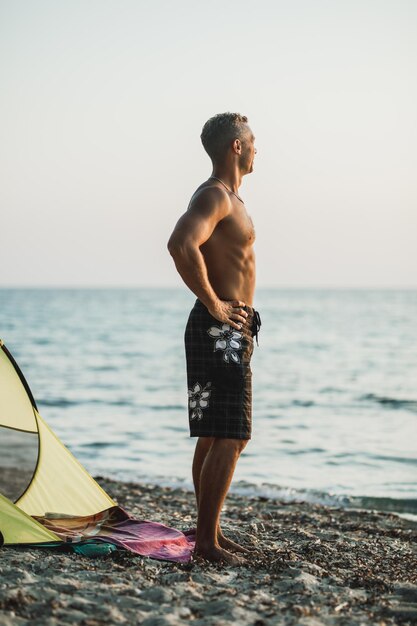 Ein gutaussehender Mann, der genießt und beobachtet, wie die Sonne am Strand untergeht.